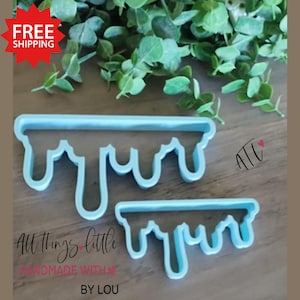 May include: Two light blue plastic cookie cutters in a dripping design. The larger cutter is above the smaller one. The text "All things little" and "handmade with love by Lou" is printed on the bottom of the image.