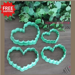 May include: Four light green heart-shaped cookie cutters with scalloped edges are displayed. The cutters vary in size, with the largest at the top left and the smallest at the top right. The image includes text that reads "All things little" and "Handmade with love by Lou".