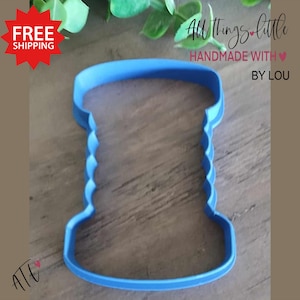 May include: Blue plastic cookie cutter shaped like a cake with a scalloped edge.  The cutter is on a wooden surface.  All Things Little Handmade With Love By Lou.