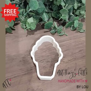 May include: A white plastic ice cream cone cookie cutter. The cutter is in the shape of an ice cream cone with a scalloped top. The words "All Things Little" and "Handmade with Love by Lou" are in the image.