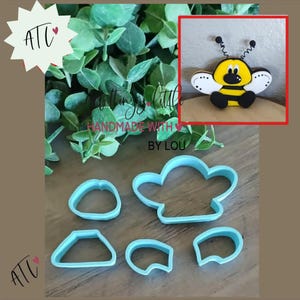 May include: A set of five light blue plastic cookie cutters in various shapes, including a large bee-shaped outline and four smaller geometric pieces, accompanied by a small decorative bee figure with yellow, black, and white details.
