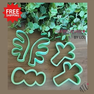 May include: A collection of light green plastic cookie cutters in various shapes, including antlers, clouds, and crosses. The phrase "All Things Little Handmade With Love By Lou" is visible in the background. The image also includes a red starburst with the text "FREE SHIPPING".