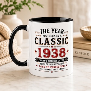 May include: A white ceramic mug with a black handle and interior rim. The front features black and red text reading: THE YEAR YOU BECAME A CLASSIC 1938, SUSAN'S BIRTHDAY EDITION, BORN ON JANUARY 8, 1938, AGED TO PERFECTION, STILL ICONIC. STILL LOVED.