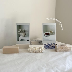 May include: A collection of decorative photo frames and place card holders. The frames display images of flowers and food. The place card holders are made of wood, marble, and floral designs. The text "Personalised prints" is visible.