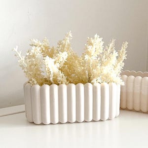 Peut inclure: Ensemble de trois mugs en céramique avec une finition mate et mouchetée. Les tasses sont de couleur crème, gris clair et gris foncé. Chaque mug a un design simple et minimaliste.
