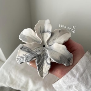 May include: A flower-shaped incense holder with a white and grey marbled pattern. The object features six curved petals and a small circular hole in the center for incense sticks. The text "Light marble" is printed in white near the top right.