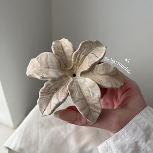 May include: A flower-shaped object with a beige marble swirl pattern. The piece features six distinct petals radiating from a central point with a small circular hole. The text "Beige marble" is printed in white on the right side of the object.