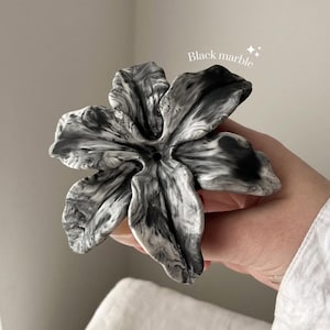 May include: A flower-shaped object with a black and white marbled pattern. The piece features five distinct, curved petals radiating from a central point with a small hole. The text "Black marble" is printed in white above the object.