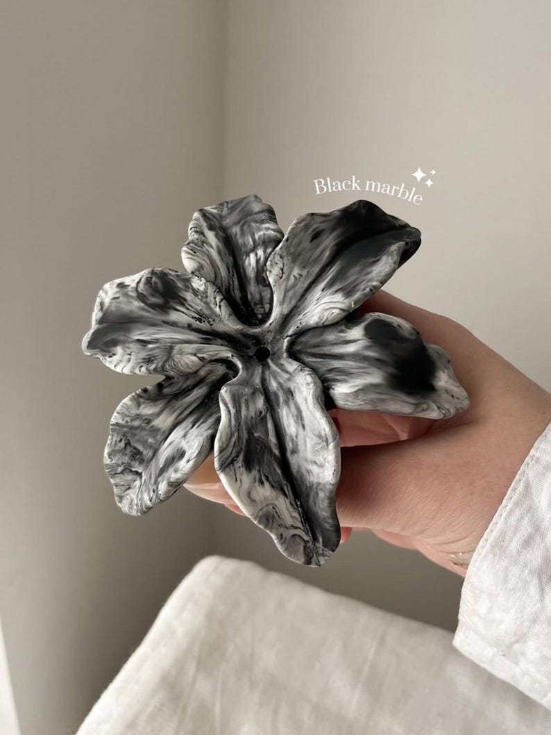 May include: A flower-shaped object with a black and white marbled pattern. The piece features five distinct, curved petals radiating from a central point with a small hole. The text "Black marble" is printed in white above the object.