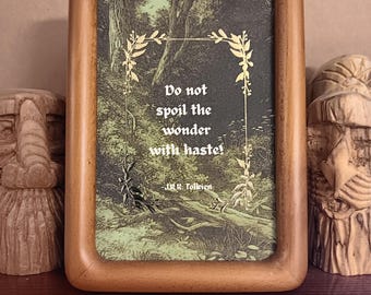 Op de afbeelding: Een houten fotolijst met een citaat van J.R.R. Tolkien. De print toont de tekst "Do not spoil the wonder with haste!" tegen een bosachtergrond. De lijst is bruin en heeft decoratieve elementen.
