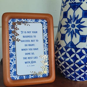 May include: A framed print with a quote by C.S. Lewis, featuring a blue floral design and gold accents. The wooden frame surrounds the print, which reads: "It is not your business to succeed, but to do right; when you have done so, the rest lies with God."