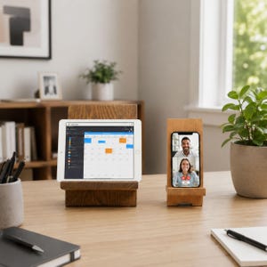 May include: A dark wood tablet stand holding a white tablet displaying a calendar interface and a light wood phone stand holding a smartphone showing a video call with two people. The stands are positioned on a wooden desk surface.