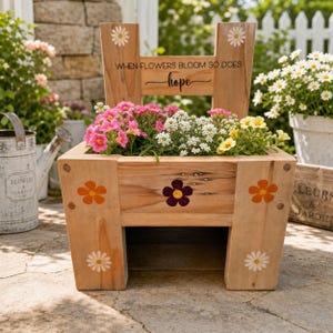 May include: Wooden chair-shaped planter box filled with pink, white, and yellow flowers. The planter features daisy and flower decals. Text on the back reads "WHEN FLOWERS BLOOM SO DOES hope."