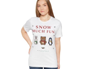 May include: A white short-sleeve t-shirt featuring the red text SNOW MUCH FUN, small snowflake icons, and a graphic of a white rabbit, a brown bear, and a penguin wearing scarves. Below the animals is a holly sprig and the text Wispling Press.