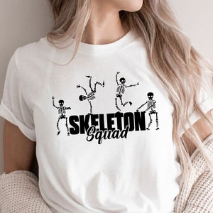 May include: White t-shirt with a black graphic of four skeletons dancing and the text "Skeleton Squad".