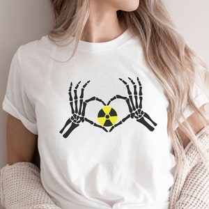 May include: White t-shirt with a black skeleton hand design making a heart shape around a yellow and black radiation symbol.