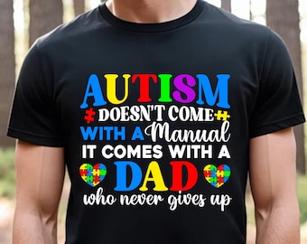 May include: Black t-shirt with a colorful autism awareness design. The text reads "Autism doesn't come with a manual, it comes with a Dad who never gives up".