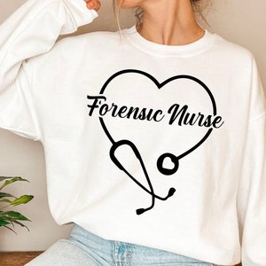 Puede incluir: Sudadera blanca con un gráfico negro de un estetoscopio en forma de corazón con el texto "Forensic Nurse" dentro del corazón.