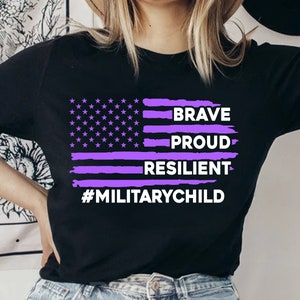 May include: Black t-shirt with a purple American flag design. The flag has the words "Brave, Proud, Resilient" and "#MilitaryChild" written on it.