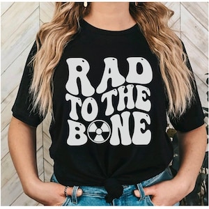 May include: Black t-shirt with a white graphic that says "RAD TO THE BONE" with a stylized radiation symbol in the "O".