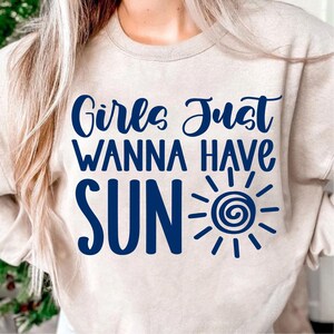 May include: A beige sweatshirt with the text "Girls Just Wanna Have Sun" in blue lettering. A stylized sun graphic is next to the text.