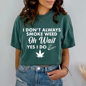 Può includere: Una maglietta verde con il testo "I don't always smoke weed Oh Wait YES I DO" in bianco. Sulla maglietta sono raffigurati anche una foglia di marijuana e uno spinello.