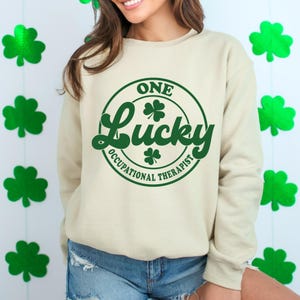 May include: A cream-colored sweatshirt with a green circle graphic that says "One Lucky Occupational Therapist".