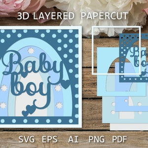 May include: A 3D layered papercut design featuring a rainbow with the words "Baby Boy" in a blue and white color scheme. The design is perfect for a baby shower or nursery decoration.