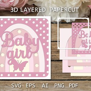 May include: A pink and white layered papercut design with a rainbow and the text "Baby girl" in a pink script font. A butterfly is in the center of the rainbow. The design is on a white background with pink polka dots.