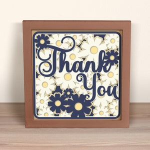 May include: A framed wood sign with a white background and a navy blue floral design. The sign says "Thank You" in a navy blue script font.