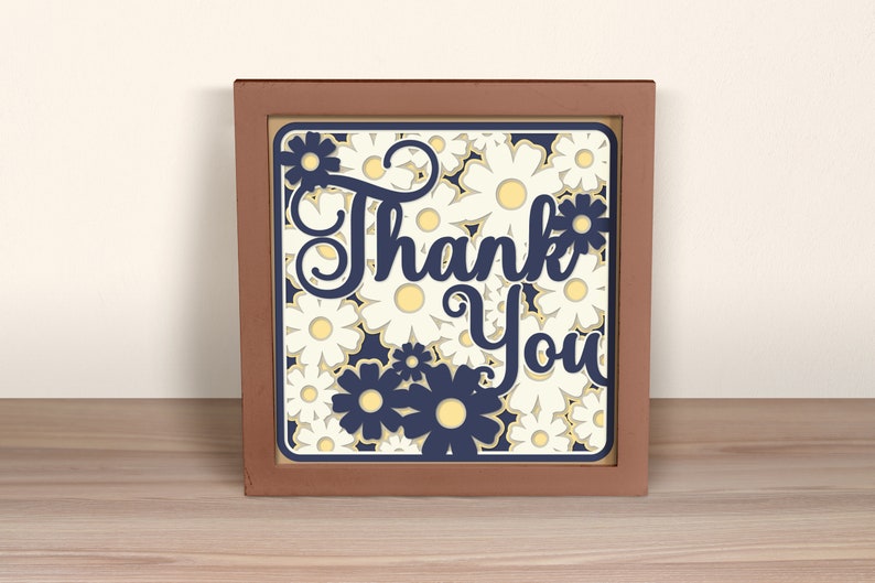May include: A framed wood sign with a white background and a navy blue floral design. The sign says "Thank You" in a navy blue script font.