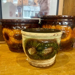 May include: Three ceramic flower pots with brown, green and yellow glaze. The pots have a raised design of flowers and leaves.