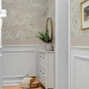 Könnte beinhalten: Ein weißer Flur mit einem hellbraunen Holzboden. Die Wände sind mit einer hellrosa Tapete mit einem weißen Wolkenmuster bedeckt. Ein weißer Schrank mit vier Schubladen steht in der Ecke des Flurs. Eine kleine Topfpflanze steht auf dem Schrank. Ein runder goldener Spiegel hängt an der Wand über dem Schrank. Ein geflochtener Korb steht auf dem Boden neben dem Schrank.
