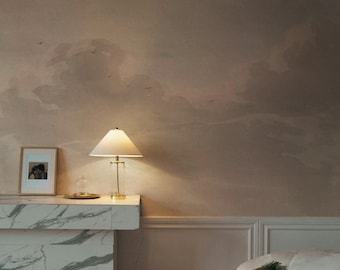 May include: A white marble console table with a lamp and a framed photo on top. The wall behind the table is painted with a light brown and beige abstract cloud design.
