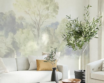May include: A light wood coffee table with a bowl of decorative items on top. The table is in a living room with a white couch and a large olive tree in the background. The wall behind the couch has a watercolor mural of a forest scene.