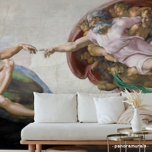 Puede incluir: Un sofá blanco con cojines blancos y una mesa auxiliar dorada se encuentra frente a un mural que representa "La Creación de Adán" de Miguel Ángel. El mural presenta figuras con los brazos extendidos y un estilo artístico detallado.