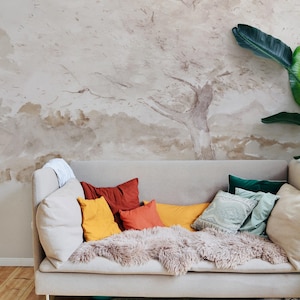 Può includere: Un divano beige chiaro con una varietà di cuscini in tonalità di arancione, giallo e verde. Il divano è decorato con una morbida coperta di pelliccia marrone e si trova di fronte a una parete con un murale ad acquerello di un albero.