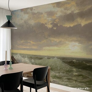 K&ouml;nnte beinhalten: Ein Esszimmer mit einem Wandbild, das eine dramatische Meereslandschaft mit tosenden Wellen unter einem bew&ouml;lkten Himmel zeigt. Der Raum umfasst einen Holztisch, schwarze St&uuml;hle und dekorative Kerzen.