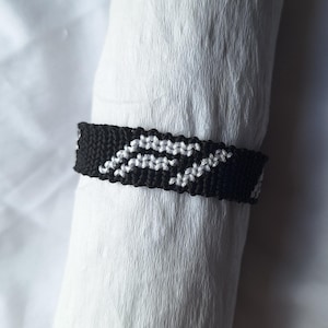 May include: Black and white friendship bracelet with a geometric pattern.