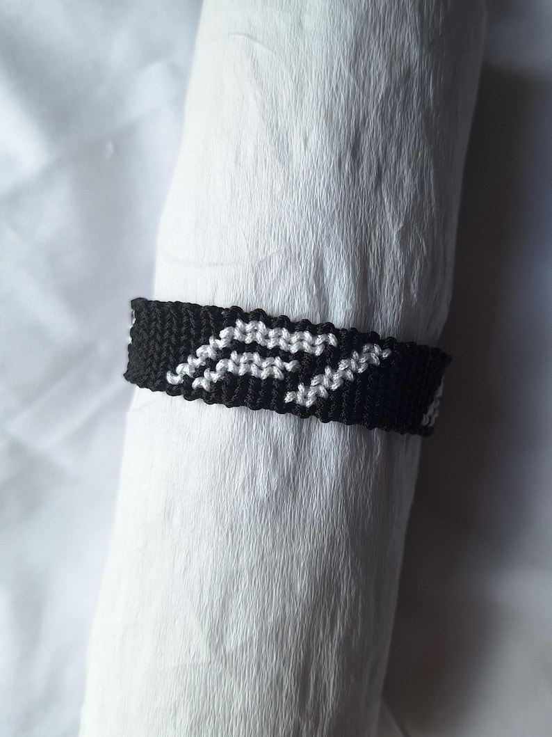 May include: Black and white friendship bracelet with a geometric pattern.
