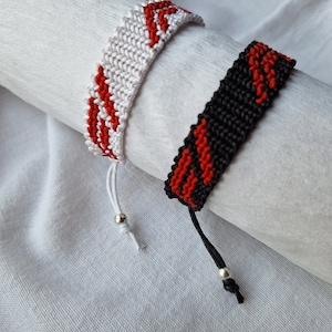 May include: Two friendship bracelets with red and white stripes and red and black stripes. The bracelets have silver beads on the ends.