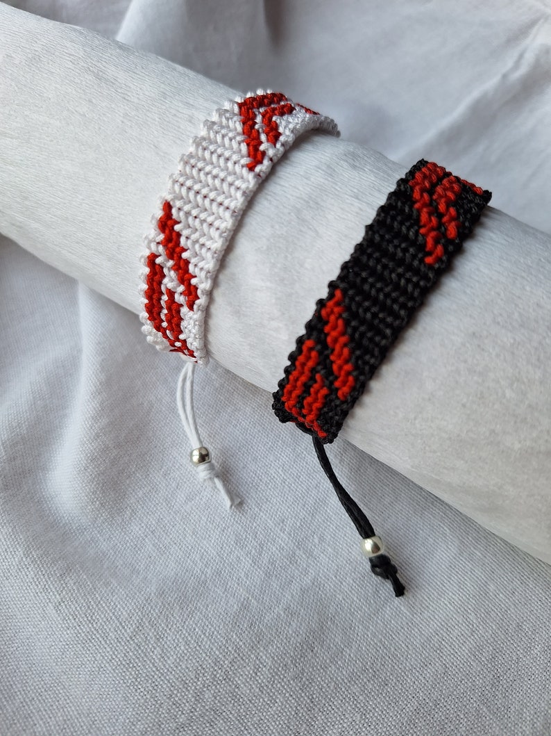 May include: Two friendship bracelets with red and white stripes and red and black stripes. The bracelets have silver beads on the ends.