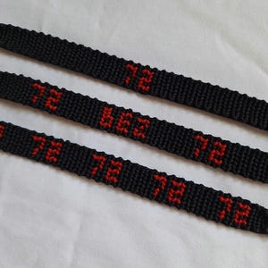 May include: Three black woven friendship bracelets featuring the number 72 stitched in red thread. The top bracelet displays the number 72 once, the middle bracelet shows the number 72 twice, and the bottom bracelet displays the number 72 three times.