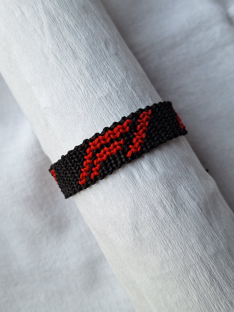 May include: A black and red friendship bracelet with a woven pattern. The bracelet is made of string and has a simple design.