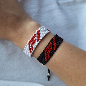 May include: Two friendship bracelets, one white with red stripes and one black with red stripes.