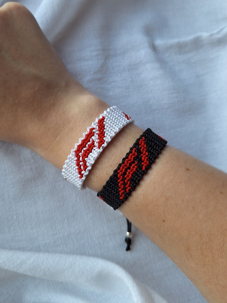 May include: Two friendship bracelets, one white with red stripes and one black with red stripes.