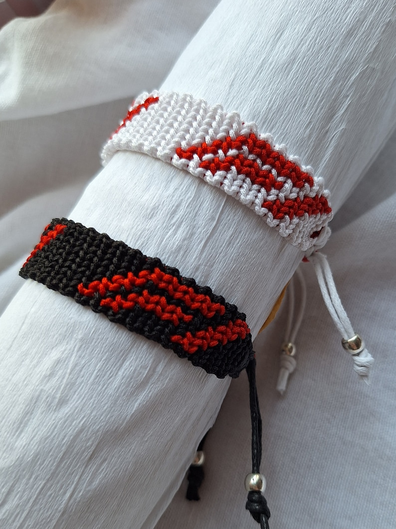 May include: Two friendship bracelets with red and white stripes and red and black stripes. The bracelets are tied with silver beads.