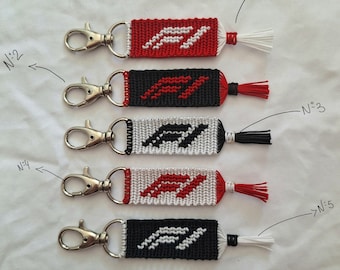May include: Five keychains with red and black woven designs. Each keychain has a silver key ring and a tassel. The tassels are white, red, black, and red. The keychains are numbered 1 through 5.
