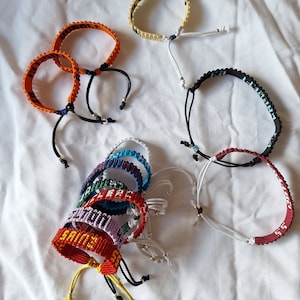 May include: A collection of colorful friendship bracelets with various words and phrases woven into the design. The bracelets are made with colorful threads and have adjustable closures.