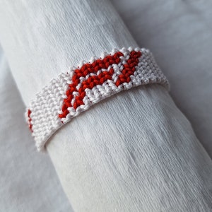 May include: White and red friendship bracelet with a chevron pattern.